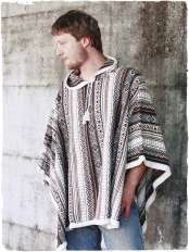 Uomo con jeans, mani in tasca davanti a un muro, indossa un poncho rettangolare di alpaca, base bianca e toni naturali, cappuccio, modello Mexico.
