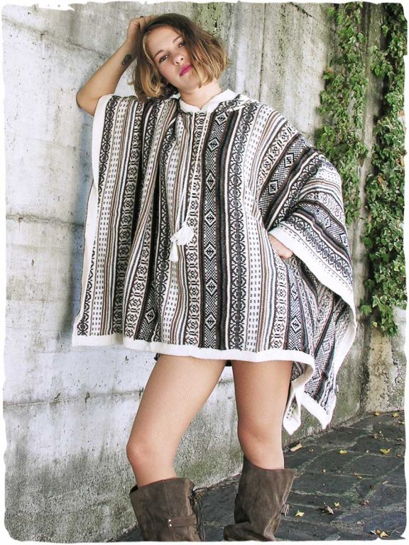 Woman by a light wall with ivy, wearing a rectangular alpaca wool poncho in natural ethnic tones, with hood, model Mexico.