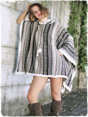 Woman by a light wall with ivy, wearing a rectangular alpaca wool poncho in natural ethnic tones, with hood, model Mexico.