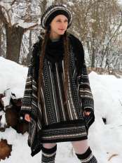 Woman with braids in a snowy landscape, wearing the alpaca poncho with jacquard pattern, black base, with matching beret, skirt and leg warmers.