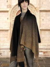 Black-haired woman wearing a black and brown baby alpaca cape shawl poncho with dotted pattern, by a carved stone doorway, model Pampa.