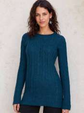Young woman with dark wavy hair and ethnic earrings, wearing a long petrol blue cable knit alpaca wool jumper, model Zora.