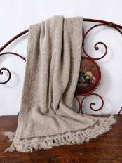 Beige alpaca wool shawl wrap with fringes, draped over an antique iron bed headboard on old wood, model Kora.